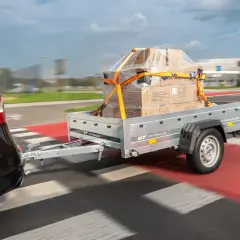 Samochód ciągnie przyczepę z zapakowanym towarem, zabezpieczonym pasami.