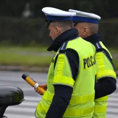 Dwóch policjantów w kamizelkach odblaskowych, jeden trzyma alkomat.