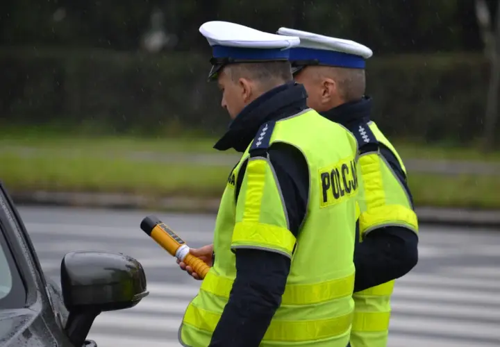 Dwóch policjantów w kamizelkach odblaskowych, jeden trzyma alkomat.