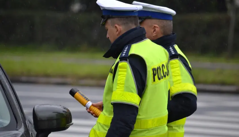 Dwóch policjantów w kamizelkach odblaskowych, jeden trzyma alkomat.