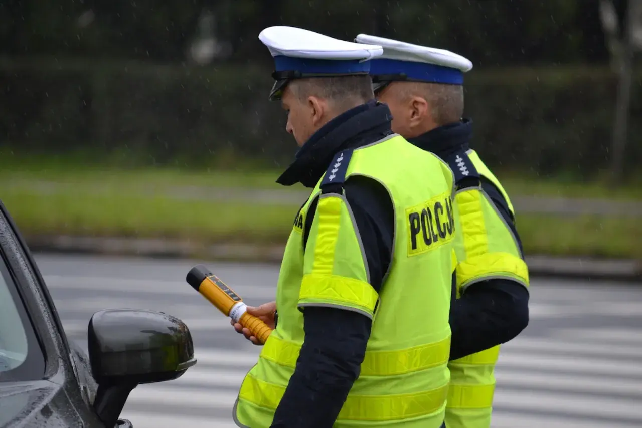 Dwóch policjantów w kamizelkach odblaskowych, jeden trzyma alkomat.